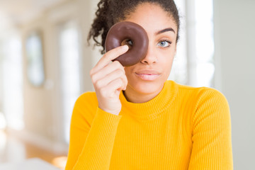 Young african american girl eating sweet chocolate donut with a confident expression on smart face...
