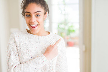 Beautiful young african american woman with afro hair wearing casual sweater cheerful with a smile of face pointing with hand and finger up to the side with happy and natural expression on face