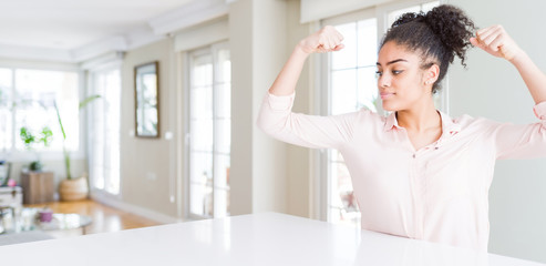 Wide angle of beautiful african american woman with afro hair showing arms muscles smiling proud. Fitness concept.