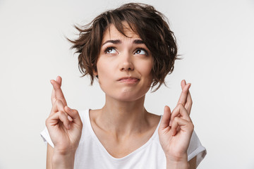 Portrait of beautiful woman with short brown hair in basic t-shirt keeping fingers crossed and...