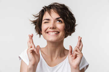 Portrait of brunette woman with short hair in basic t-shirt keeping fingers crossed and wishing...