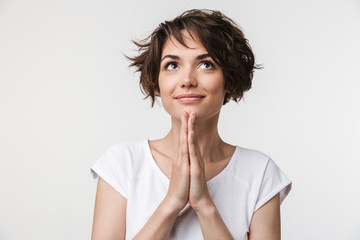 Portrait of european woman with short brown hair in basic t-shirt keeping palms together and praying