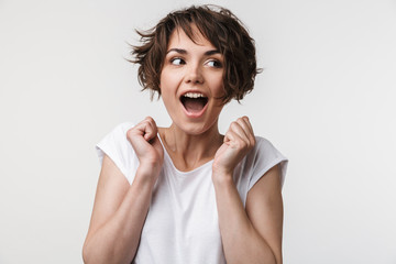Portrait of joyous woman with short brown hair in basic t-shirt rejoicing and clenching fists