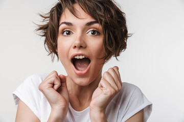 Portrait of positive woman with short brown hair in basic t-shirt rejoicing and clenching fists