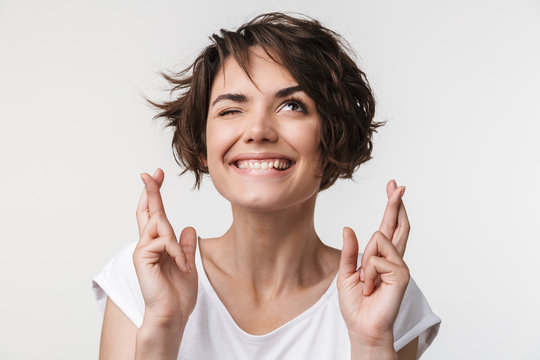 Portrait of brunette woman with short hair in basic t-shirt keeping fingers crossed and wishing good fortune