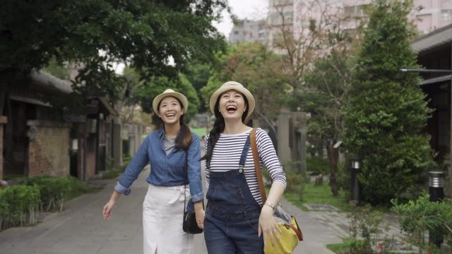 two asian girl friends walking in japanese street in tokyo japan travel trip. excited woman running fast holding hands showing sisters pointing finger to sky with amazing view surprise face.
