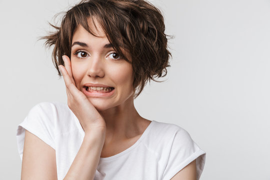Photo of excited woman with short brown hair in basic t-shirt keeping hand over her face and looking at camera