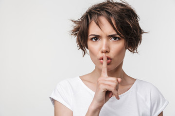 Portrait of strict woman with short brown hair in basic t-shirt holding index finger on lips