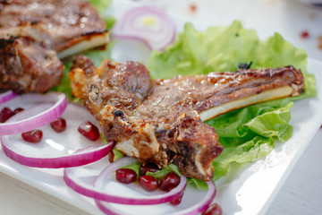 Barbecue ribs on white plate, meat dish served with onion and herbs.