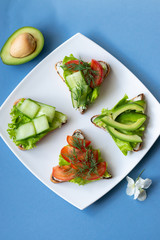 Vegetarian sandwiches with avocado, tomatoes and cucumbers on a blue background