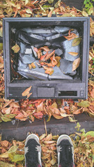 Old vintage tv with broken screen in autumn leaves