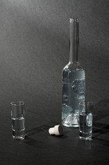 Glasflasche und Gläser mit Flüssigkeit und Korken vor dunklem Hintergrund