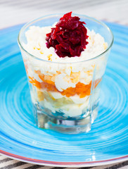 verrin glass with Russian salad herring under fur coat from vegetables on blue plate