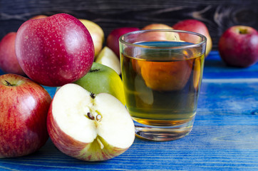 apples red and green and transparent glass of Apple juice on a wooden background side view