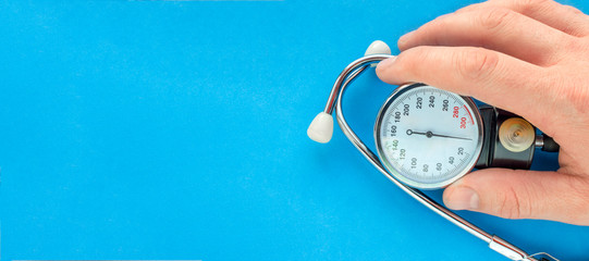 The medical manometer and stethoscope in a hand on a blue background, copy space