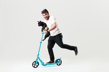 Bearded man holding a dog on electric scooter and riding it while feeling delighted. Full length portrait of an overjoyed guy riding a scooter and looking at the camera isolated on white background  © oes