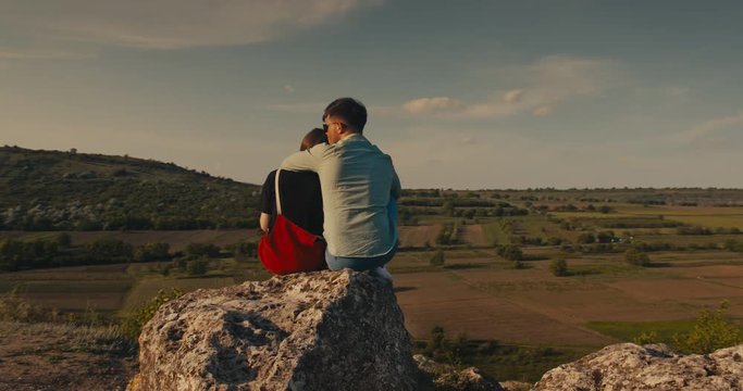 Young couple hugging while sitting on a cliff with a beautiful view.