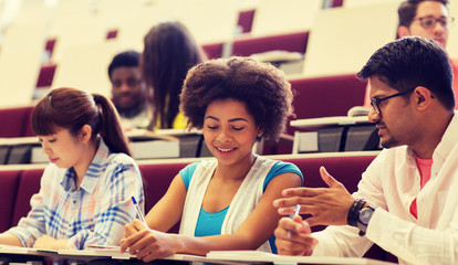 education, high school, university, learning and people concept - group of international students with notebooks writing in lecture hall