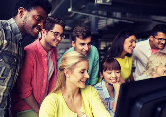 people, education, technology and school concept - group of happy smiling international students with computers at library in university