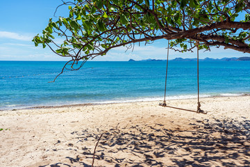 Wooden swing under tree on sand beach with blue sea