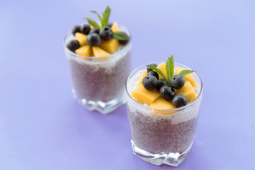 Two glasses of Chia pudding with coconut cream, mango and blueberry on blue background, top view. Healthy food, raw, vegan.