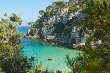 Headland on the turquoise sea with a family on a canoe in the middle of the Bay of Macarelleta