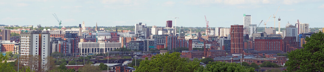 a wide panoramic view showing the whole of leeds city center with towers apartments roads and commercial buildings against a blue sky