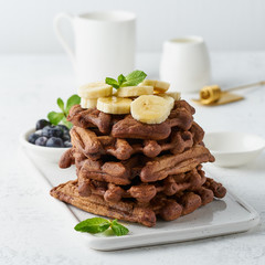 Chocolate banana waffles with maple syrup on white table, close up, side view.