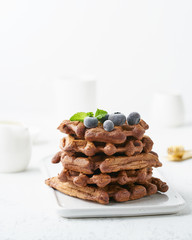 Chocolate banana waffles with blueberry on white table. Side view, vertical