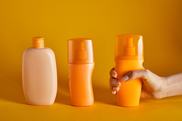 cropped view of woman holding sunscreen near cosmetics in bottles on orange background