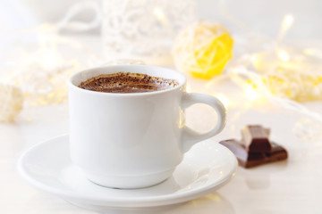 Romantic breakfast. A cup of black coffee with chocolate on a background of glowing lanterns. Postcard Design