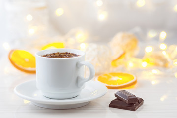 Romantic breakfast. A cup of black coffee, chocolate slices and orange slices on a background of glowing lanterns. Postcard Design