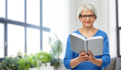 vision, wisdom and old people concept - smiling senior woman in glasses reading book over home living room background