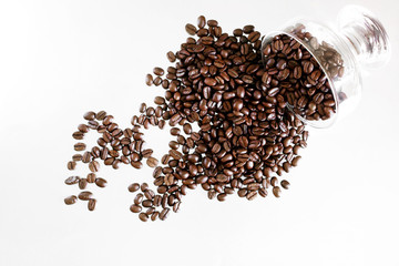 Roasted beans of Arabica coffee are poured out onto a light surface from a transparent glass bowl