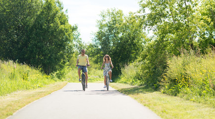 Fototapeta premium people, leisure and lifestyle concept - happy young couple riding bicycles along road in summer