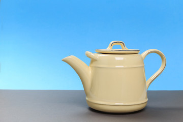 rustic yellow porcelain teapot on a gray board and a blue background