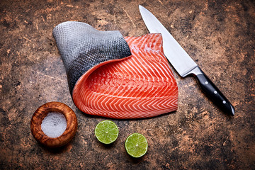Fresh salmon steak red fish on grunge background with knife and cuted lime top view. © Yasonya