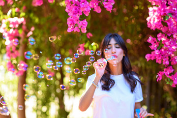 Portrait of Young woman blowing soap bubbles on pink flowers background on the beach.