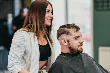 beautiful girl hairdresser cuts a bearded man in the salon