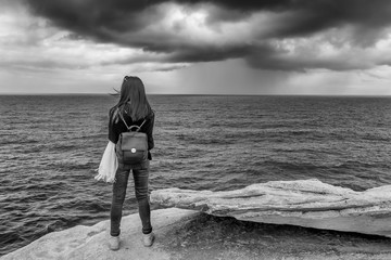 Black and white view of a girl observing the sea with a lot of wind and cloudy sky