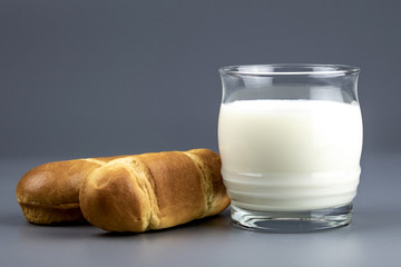 two buns next to a glass of milk on a grey