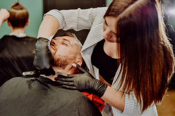 Obraz na płótnie Canvas girl hairdresser shaves his beard with a man razor