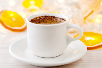 Romantic breakfast. A cup of black coffee and orange slices on a background of glowing lanterns. Postcard Design