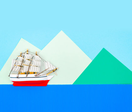 Little ship on a blue background with paper cut mountains. Copy space for text. Top view travel or vacation concept