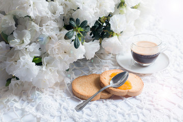 Apparecchiatura romantica del tavolo della colazione, con fiori di azalea bianca, tazza di caffè e biscotti con marmellata