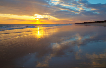 Beautiful south sunset on the sea. Deserted sandy shore of the Atlantic Ocean with the reflection of the clouds. Seascape. Natural summer background. Vilamoura, Falesia, Algarve, Portugal