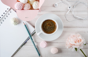 morning coffee with a notebook and a pencil, with a box filled with small meringues, headphones on a wooden light background.