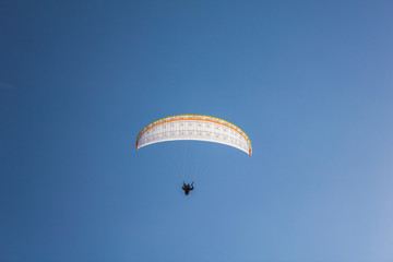 paraglider on a white parachute flies against a clean blue sky, bottom view