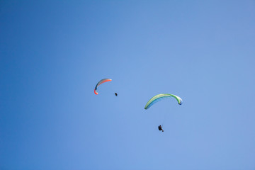 two paragliders on colored parachutes fly against a clear blue sky