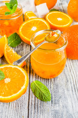 Homemade orange jam, with fresh sliced oranges and mint leaves, white wooden background copy space